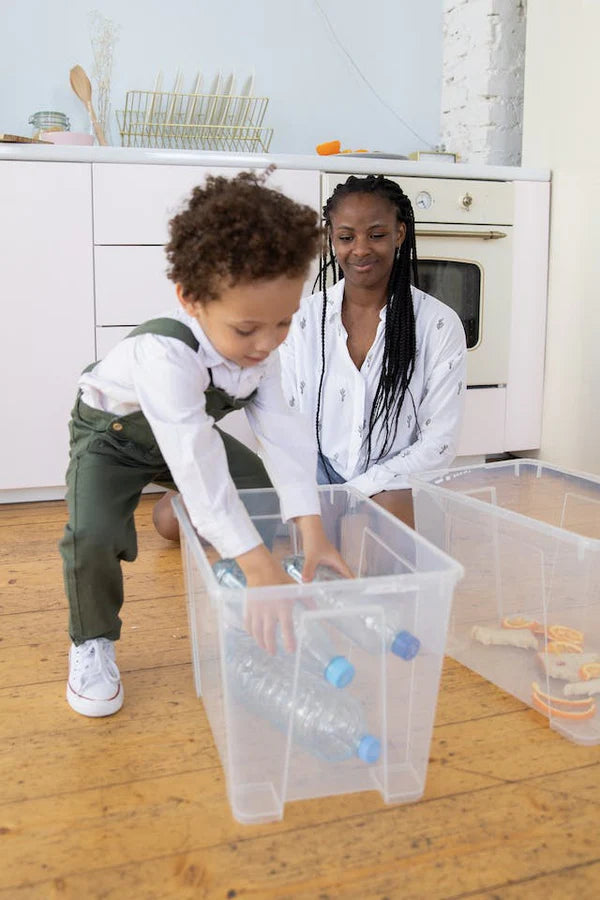 A young mother teachng watching her young child place plastic bottles into a container.