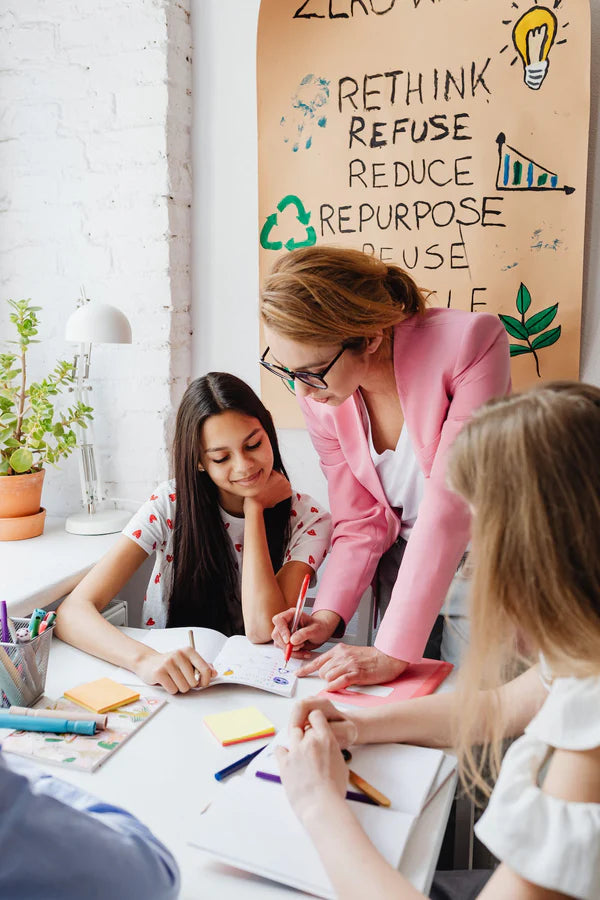 A female teacher teaching two female students about recycling.