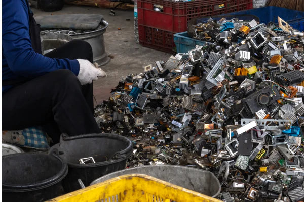 A worker in a recycling facility is sitting down sifting through a pile of electronic waste.
