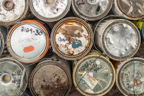 Closeup of cans of paint that look to be used--most of the cans are rusted and dented.