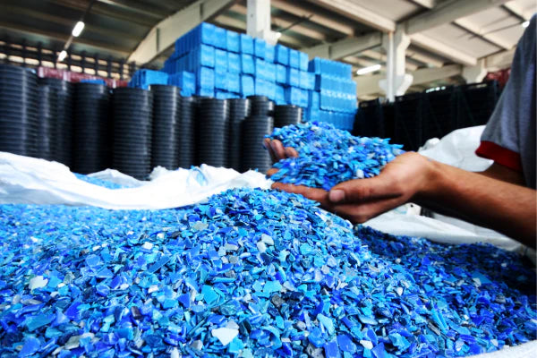 Raw materials produced by recycling household items. The raw materials are blue in colour and look like plastic chips. A human has scooped up a pile of the recycled plastic materials in their hands.