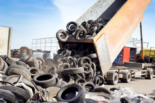 A semi truck unloading a large bin full of car tires.