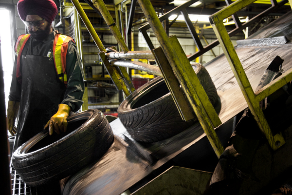A worker in a recycling plant moving a used tire off of a conveyor belt.