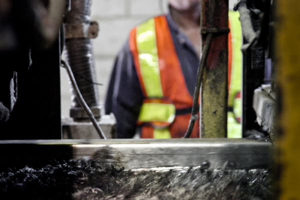 A closeup of some machinery in a tire recycling plant.  The operator of the machinery observes the machine while it operates.