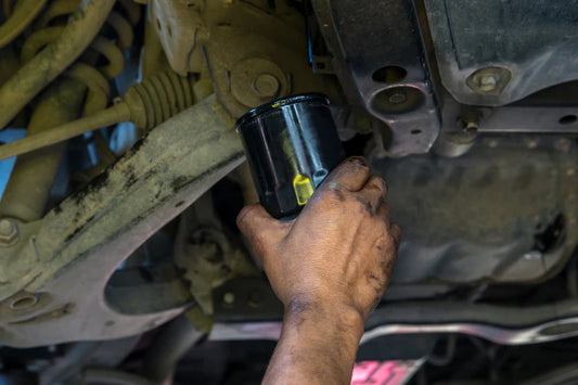 Closeup of a hand removing an oil filter from a the underside of a car.