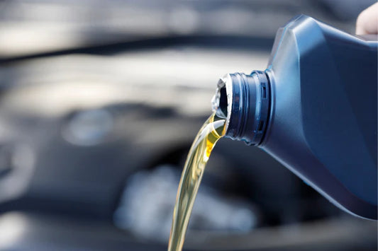 A close up of oil being poured into an engine from an oil container.