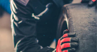 A man rolling a tired. The man is wearing red gloves and is wearing coveralls.